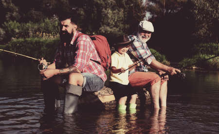 Father, son and grandfather fishing. Men day. Great-grandfather and great-grandson. Fly fishing for trout. Father and son fishing.の写真素材