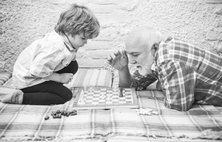 Senior man teaching his grandson to play chess. Handsome grandpa and grandson are playing chess while spending time together at home.の写真素材