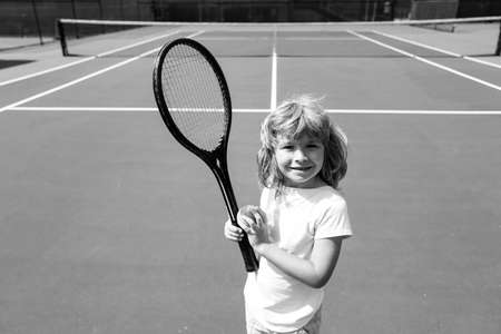 Child boy tennis beginner player on outdoor tennis court.
