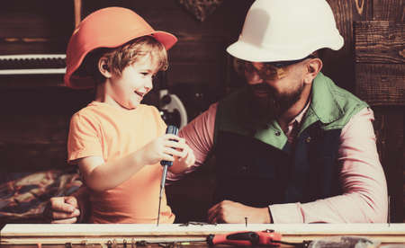 Little son helping his father with building work. Parent in protective helmet teaching little son to use different tools in school workshop.の写真素材
