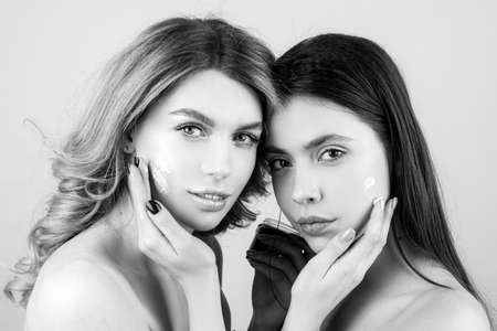 Spa woman applying facial clay mask. Two beauty women with facial masks having fun on studio background isolated. Facial mask, spa procedure.の写真素材