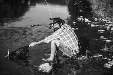 Man in shirts fishing with net and rod during the morning light on the lake. Fish on hook. Fisher...