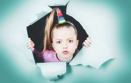 Child girl looking out of a paper hole. Banner. Happy girl. View of girl face through hole in blue...