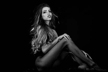 Sexy seductive woman with luxury makeup and long blonde curly hair posing at camera. Sexy hot girl with long slim legs wearing fishnet tights. Woman glamour and style concept.の写真素材