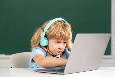 Angry sad child boy in headphones using a laptop and study online with video call teacher at school....