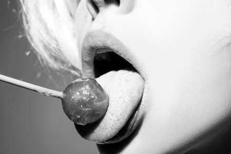 Licking candy. Lollipop model. Woman lips sucking a candy. Glamor sensual model with red lips eat sweats lolly pop.の写真素材