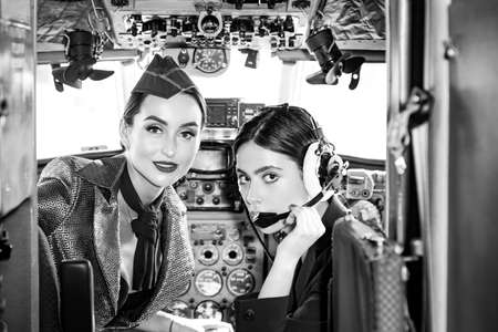 Trainee Pilot and Flight Instructor in an Aircraft Cockpit. Wishes a successful flight. Young girls in aircraft. Pilots in cockpit. Woman holding aviator headset and looking at camera. Woman co-pilot.の写真素材