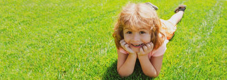 Banner with spring child face. Kids laying in grass, cute child in summer nature park. Kids on green grass background.の写真素材