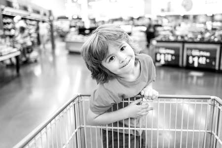 Funny customer boy child holdind trolley, shopping at supermarket, grocery store.の写真素材