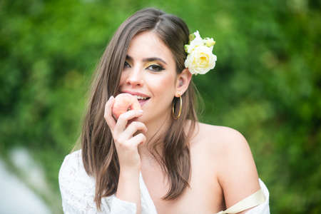 Sexy girl on summer picnic on a grass in the park. Outdoor fashion photo of beautiful young woman with rose in hair eating peach.の写真素材