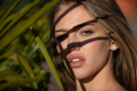Portrait of beautiful woman with shadows of palm leaf on face. Young beautiful woman with shadow of...