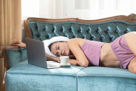Young attractive woman with coffee and laptop relaxing at home. Cozy lazy mornig. Beautiful girl in...