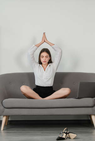 Secretary woman doing yoga exercise on sofa at workplace in a modern office. Pretty accountant girl meditating on office. Successful female manager, beautiful secretary girl.の写真素材