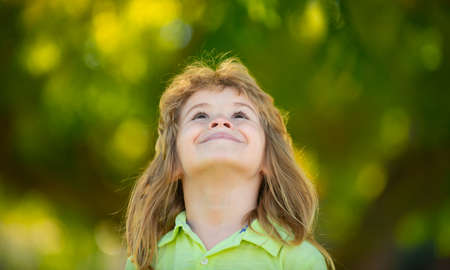 Close up portrait of cute boy looking up outdoors. Closeup headshot portrait of smiling little boy on nature background, happy small preschooler child.の写真素材
