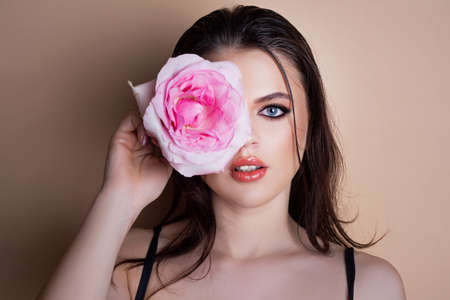 Portrait of a woman with a rose flower. Beauty fashion model woman face. Portrait of a beautiful young girl with a pink rose near face.の写真素材