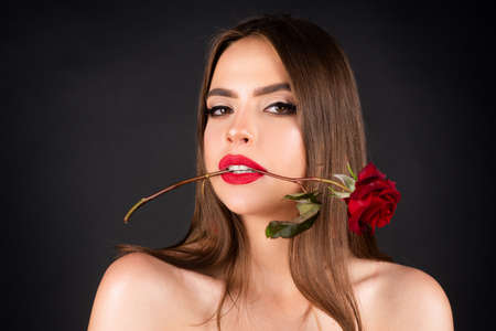Seductive sensual woman holding red rose with teeth. Close-up portrait of young beautiful sexy woman with red rose. Birthday day.の写真素材