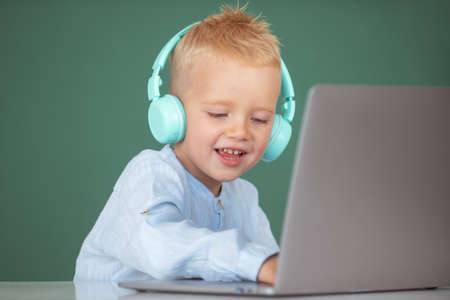 Clever school boy, cute pupil wears headphones writing on laptop, listen audio lesson use computer....