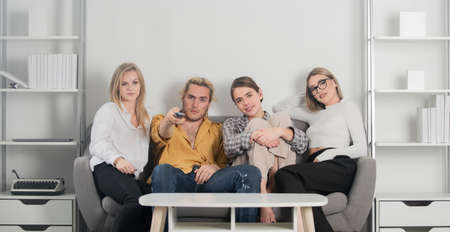 Group of young people sitting on sofa and talking at home. Friends watching TV in evening at home.の写真素材