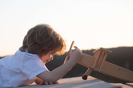 Little boy with wooden plane, boy wants to become pilot and astronaut. Happy child play with toy airplane. Kids pilot dreams of flying. Childhood dream imagination concept.の写真素材