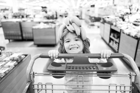 Child with shopping cart at grocery store or supermarket. Kid buying banana fruit in grocery market.の写真素材