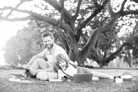 Outdoor education. Father and son use laptop, dad and school boy child looking tablet. Outdoor...
