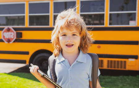 Smart schoolboy with digital tablet at school park near school bus. Education and learning for kids.
