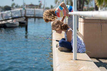 Two kids boy and girl fishing in a river or lake. Happy excited surprised amazed children friends fishing together near the pond with fishrods.の写真素材