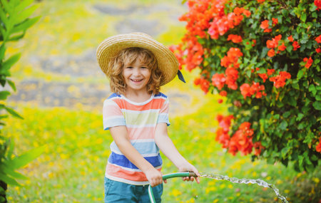 Cute child in straw hat is laughing with water spraying hose.の写真素材