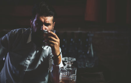 Young man holding glass of whiskey. Guy with beard holds brandy. Bearded drink cognac. Sommelier tastes drink. Man holding a glass of whisky. Sipping whiskey. Degustation, tastingの写真素材