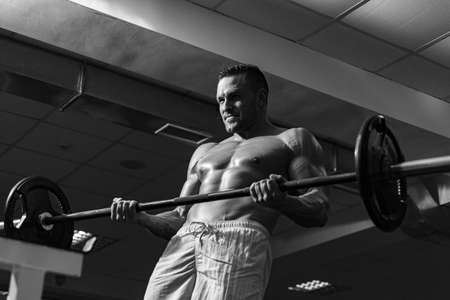 Muscular man doing crossfit. Fit man doing biceps lifting barbell. Young man working out at crossfit gym. Athletic guy doing exercise.の写真素材