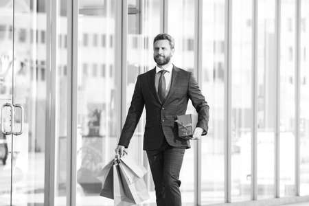 Rich man. Business man shopping in a shopping center. Happy businessman in suit holding paperbags. Shopaholic man walking on commercial street with a lot of shopping bags.の写真素材