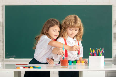 School children drawing a colorful pictures with pencil crayons in classroom. Portrait of cute...