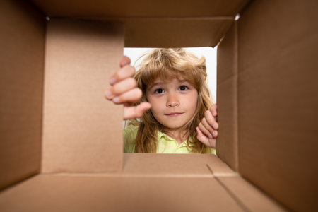 Surprised child boy unpacking, opening carton box and looking inside. The package, delivery,...