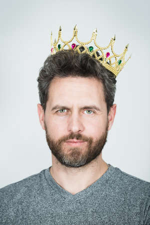 Young man with golden crown of king over gray background. Handsome successful man wearing king crown. King of style. The concept of leadership, excellence.の写真素材