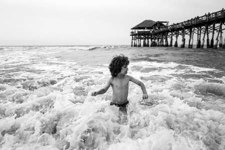 Happy child playing in the sea on sunset. Kid playing in outdoor jumping into water on summer...