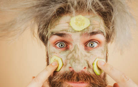 Close up Funny man with clay mask and cucumber slices on face. Male spa, dermatology, wellness and...