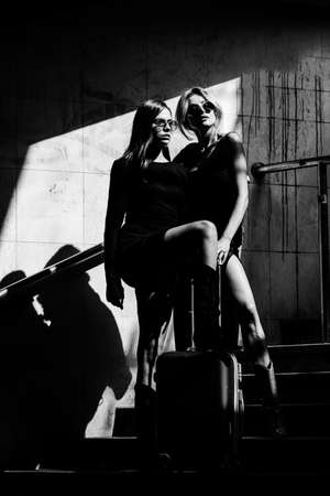 Fashionable woman couple lesbians on the street, fashion street style. Traveling with suitcase.の写真素材