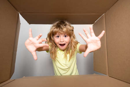 Child opens carton box and pulling out gift from it. Small boy looking in parcel box and happy to...