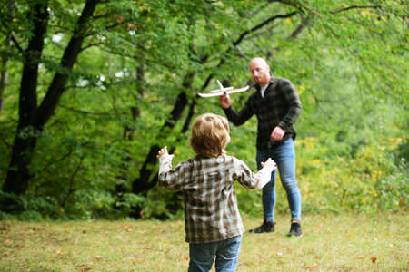 Cute child with dad play with toy plane. Fathers day. Dad and baby son playing together outdoors toy...