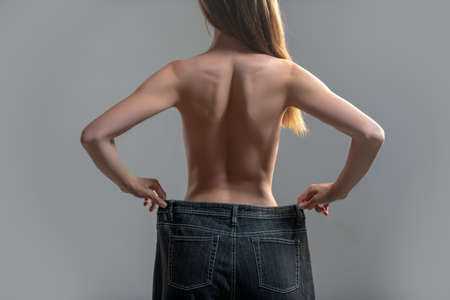 Woman showing weight lost. Slim girl wearing oversized pants. Woman shows weight loss. Dieting. Woman showing slim body after sport trainings, healthy eating.の写真素材