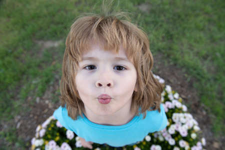 Charming blond child on background of flowers in summer. Pretty little child working in garden, child taking care of flowers, enjoying warm and sunny day.の写真素材