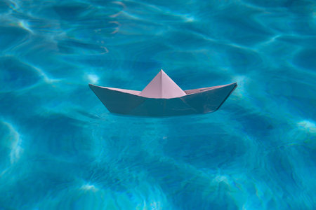 Paper boat sailing on water causing waves and ripples. Paper boat into water. Concept of tourism, travel dreams vacation holiday. Blue water background.の写真素材