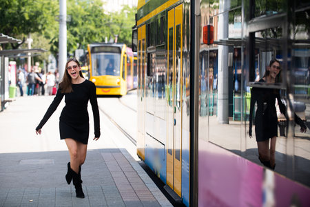 Fashionable woman running after bus trolleybus and pulling trolley case on the street, fashion...