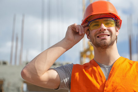 Portrait of positive male builder in hardhat working at construction site. Builder worker in helmet...