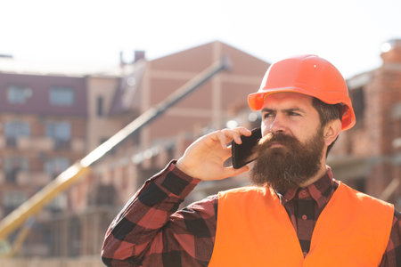 Portrait of man builder in hardhat working at construction site, talking on phone. Portrait of...