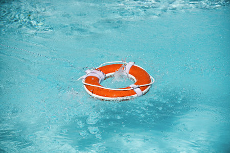 Lifebelt on sea or pool. Orange inflatable ring floating in blue water. Life buoy for protect and...