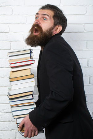 Funny teacher or professor with book stack. Thinking serious mature teacher. Falling books concept. Mature professor, middle aged teacher, bearded fun man. Books stacked fall.の写真素材