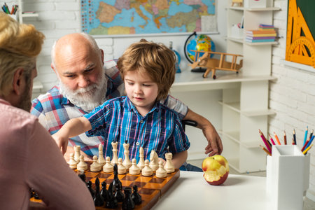Father and son playing chess. Happy smiling grandson boy with dad and granddad learning together. Happy family. Three men generation, grandfather father and son.の写真素材