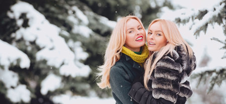 Happy winter woman friends hugging on winter snowy background outdoor. Portrait of young beautiful women couple having fun. Models walking in winter street. Female winter fashion concept.の写真素材
