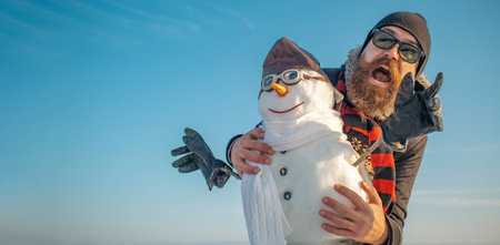 Excited man with snowman on winter outdoor background. Snow man for winter banner.の写真素材